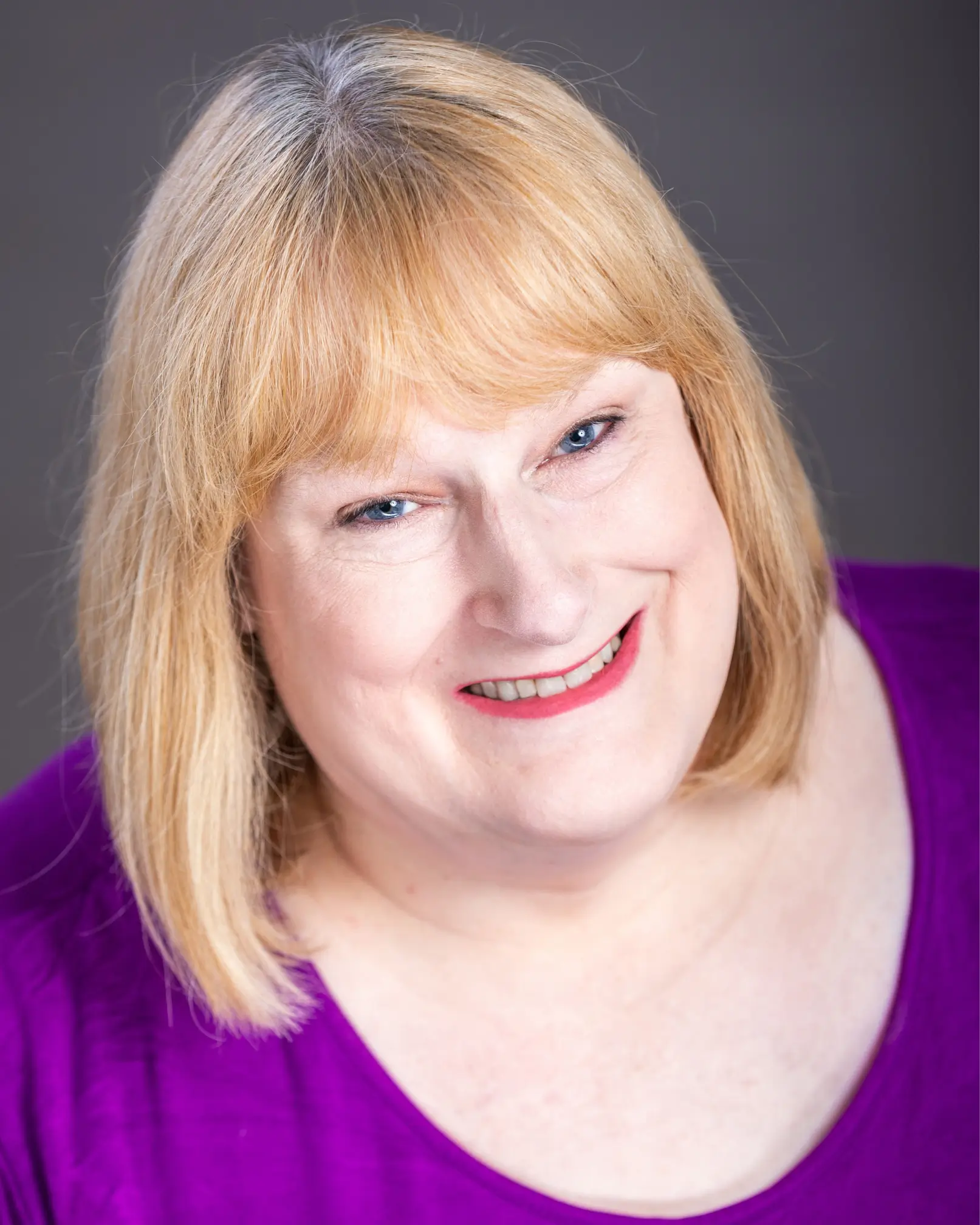 Headshot photo of actress Annie Wallace. Annie has blonde hair in a bob style and is wearing a blue top.